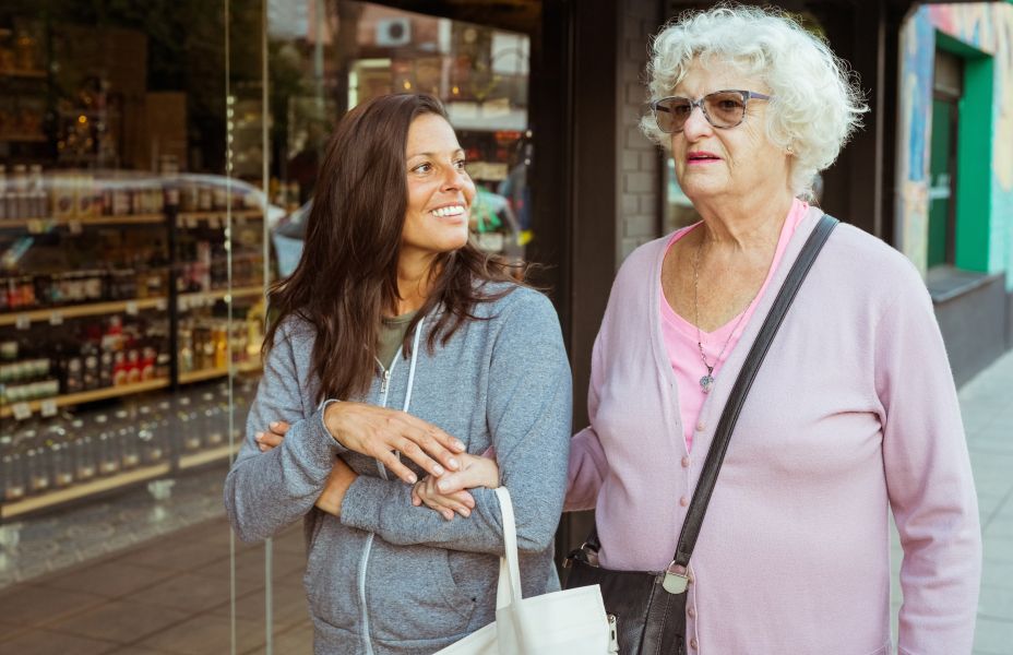 Smiling senior woman going to shopping with female, walking footpath arm in arm in the town